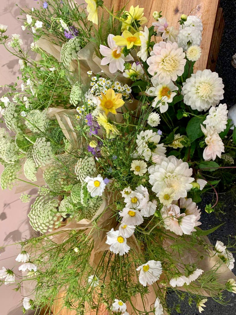 Blomsterbøtte med blomster i hvitt, gult og bittelitt blått klar for bryllup